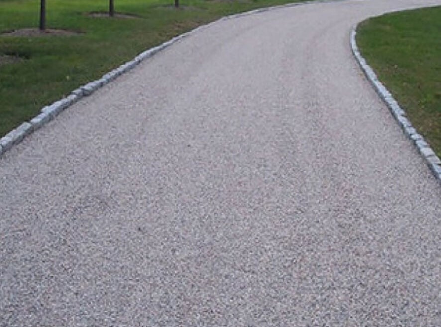 A gently curving gravel path bordered by short stone edges runs through a grassy area with small trees spaced evenly along the sides, offering a charming contrast to nearby driveway asphalt or commercial asphalt surfaces in Wilson County.
