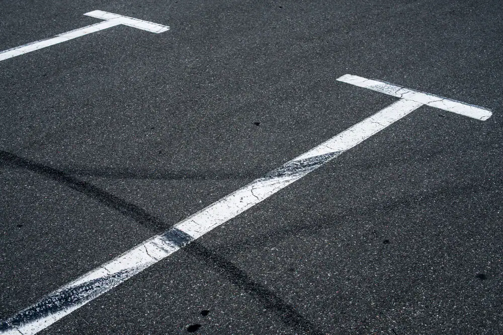 White parking lines on an asphalt surface, with black tire marks crossing over them, indicating use and wear in the parking area.